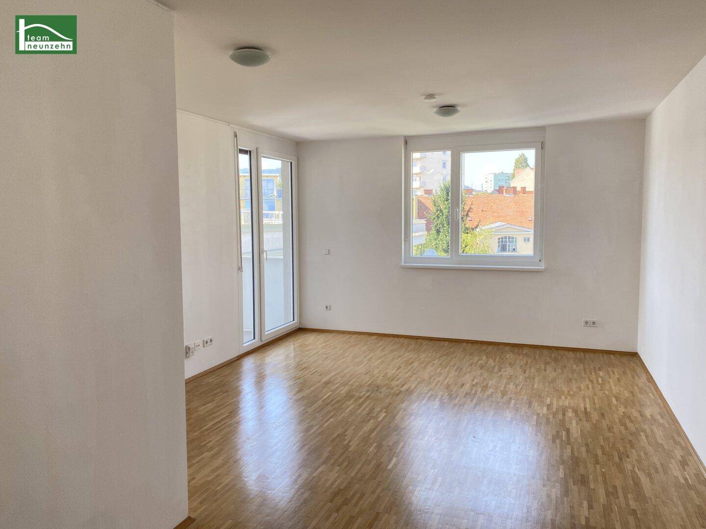 Geräumiges, leeres Wohnzimmer mit Holzboden und Zugang zu einem Balkon.