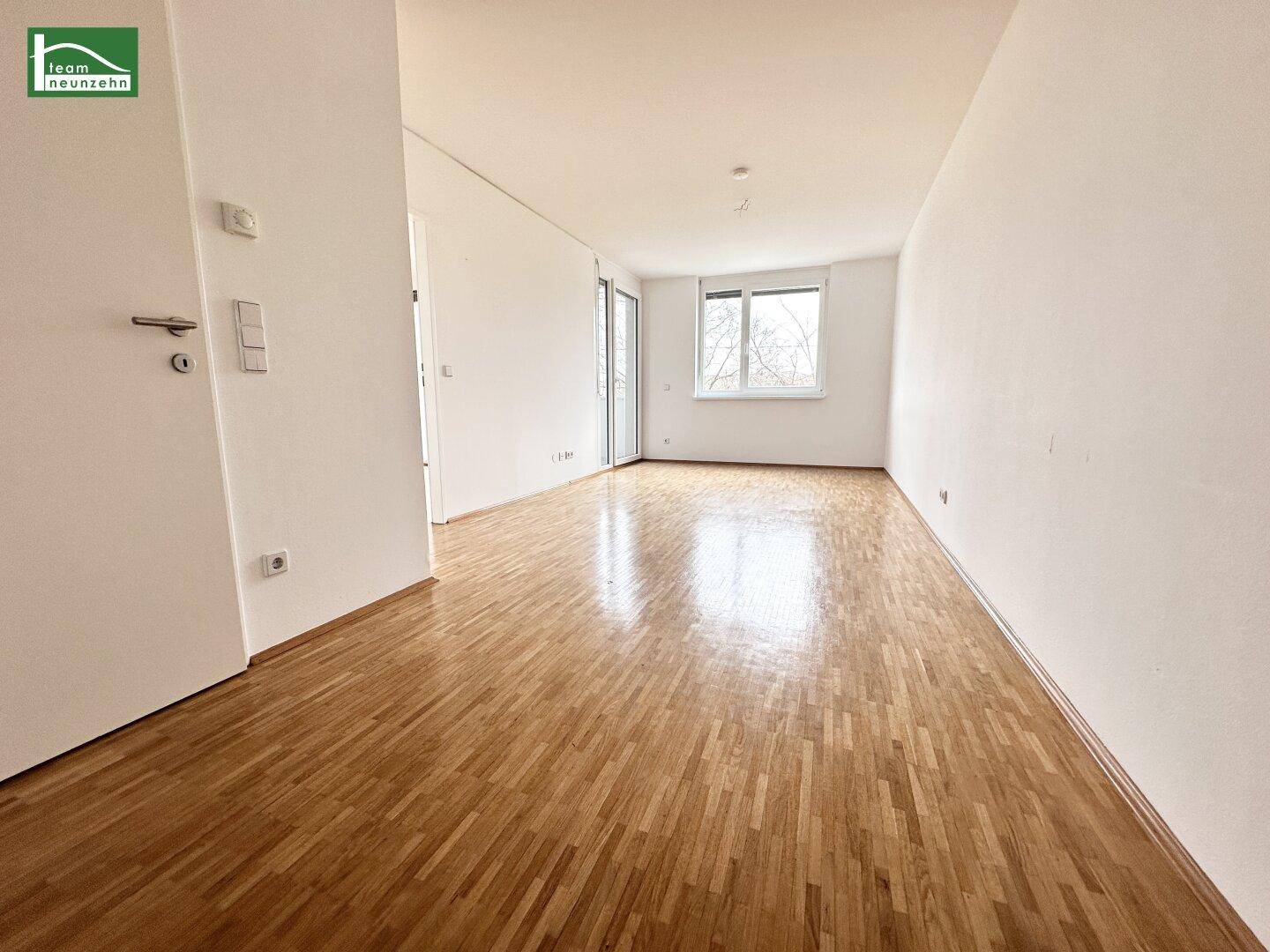 Heller, leerer Raum mit Holzboden und großen Fenstern, ideal für Wohnbereich.