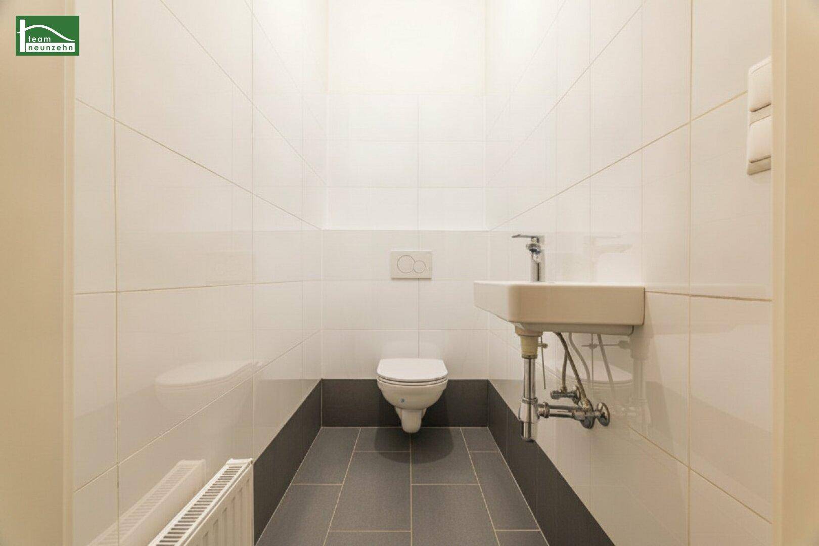 Modernes Gäste-WC mit weißen Wandfliesen, dunklem Fliesenboden und wandhängendem WC.