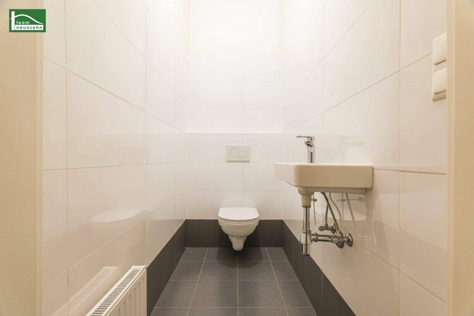Modernes Gäste-WC mit weißen Wandfliesen, dunklem Boden und wandhängendem WC.