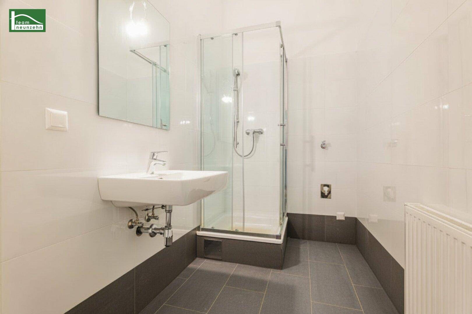 Helles Badezimmer mit moderner Duschkabine, Waschbecken und weißen Wandfliesen.