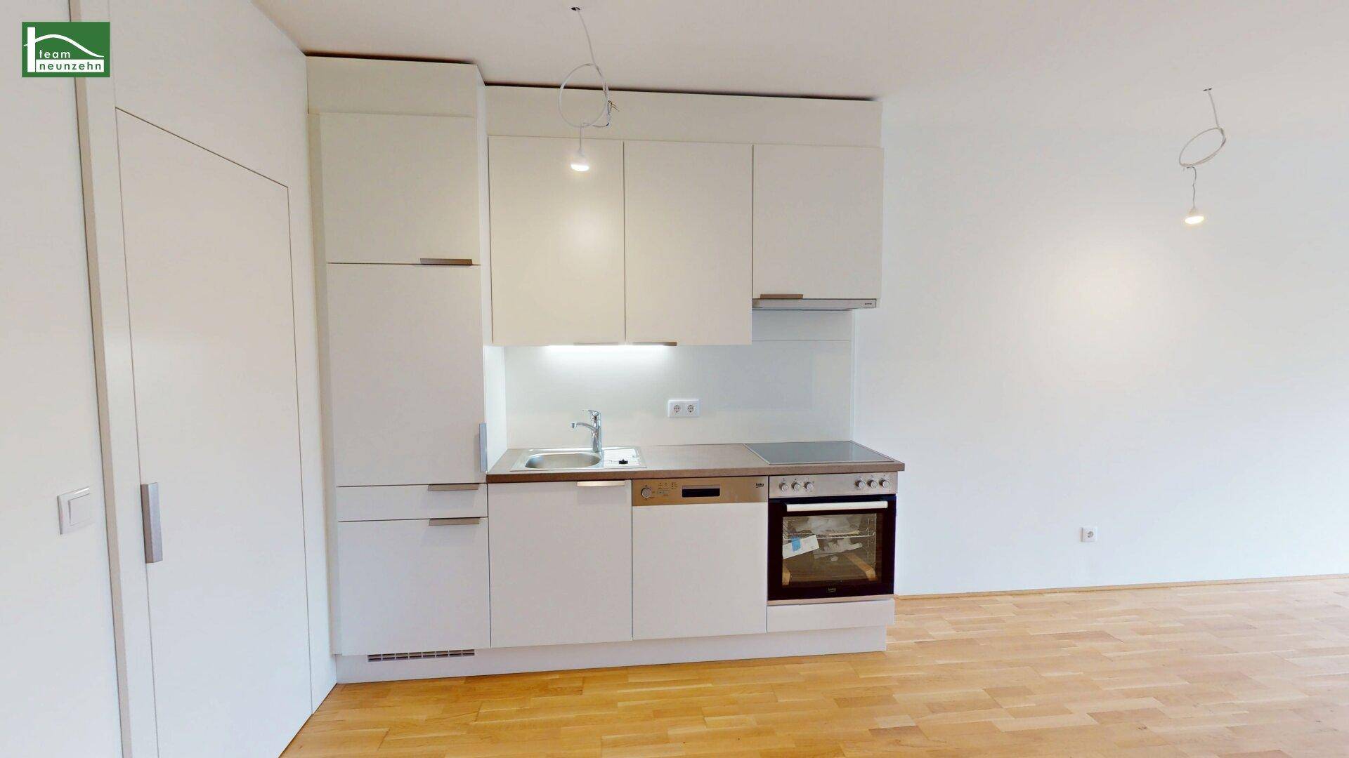 Kleine, moderne Küchenzeile mit weißen Schränken und integrierten Geräten.