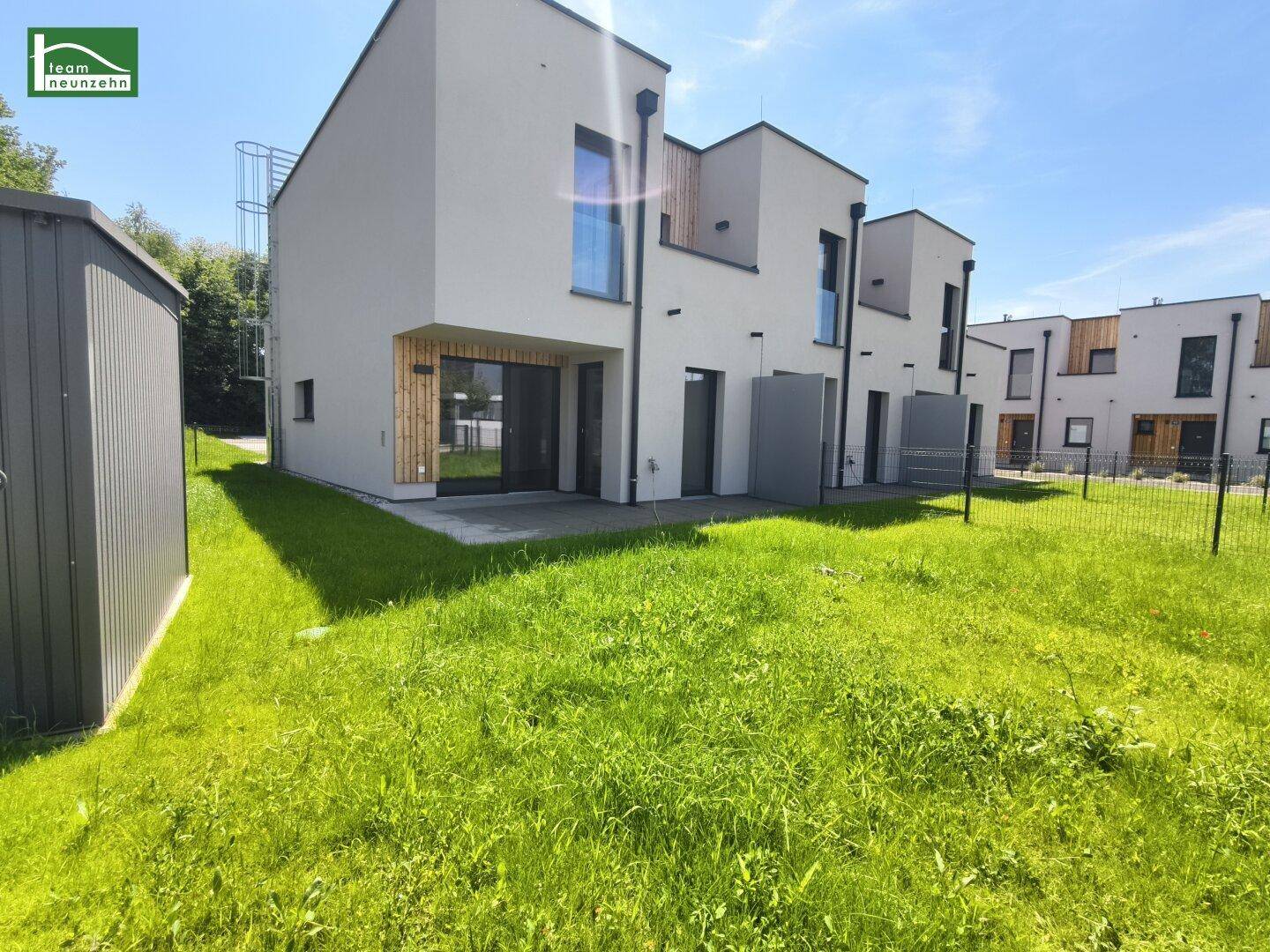 Moderne Reihenhäuser mit weißer Fassade, Holzdetails und großzügigen Glasfronten, umgeben von einer grünen Rasenfläche.