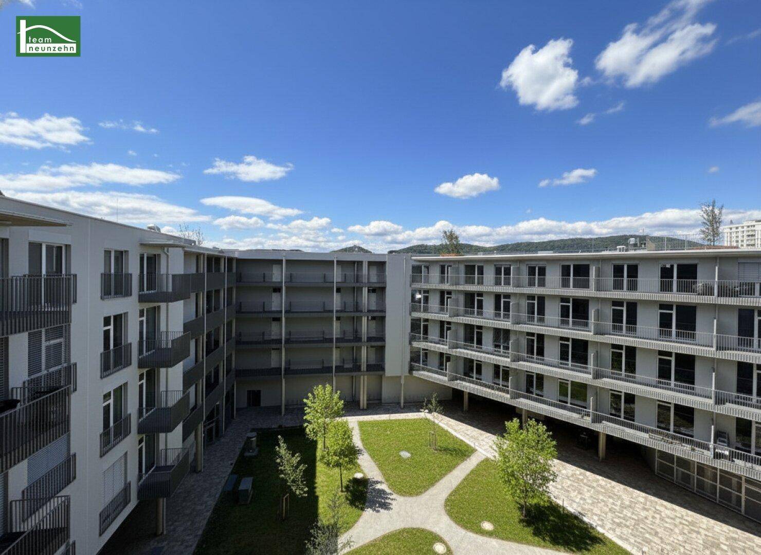 Grüner Innenhof des Wohnkomplexes mit gepflegten Rasenflächen und umliegenden Balkonen.