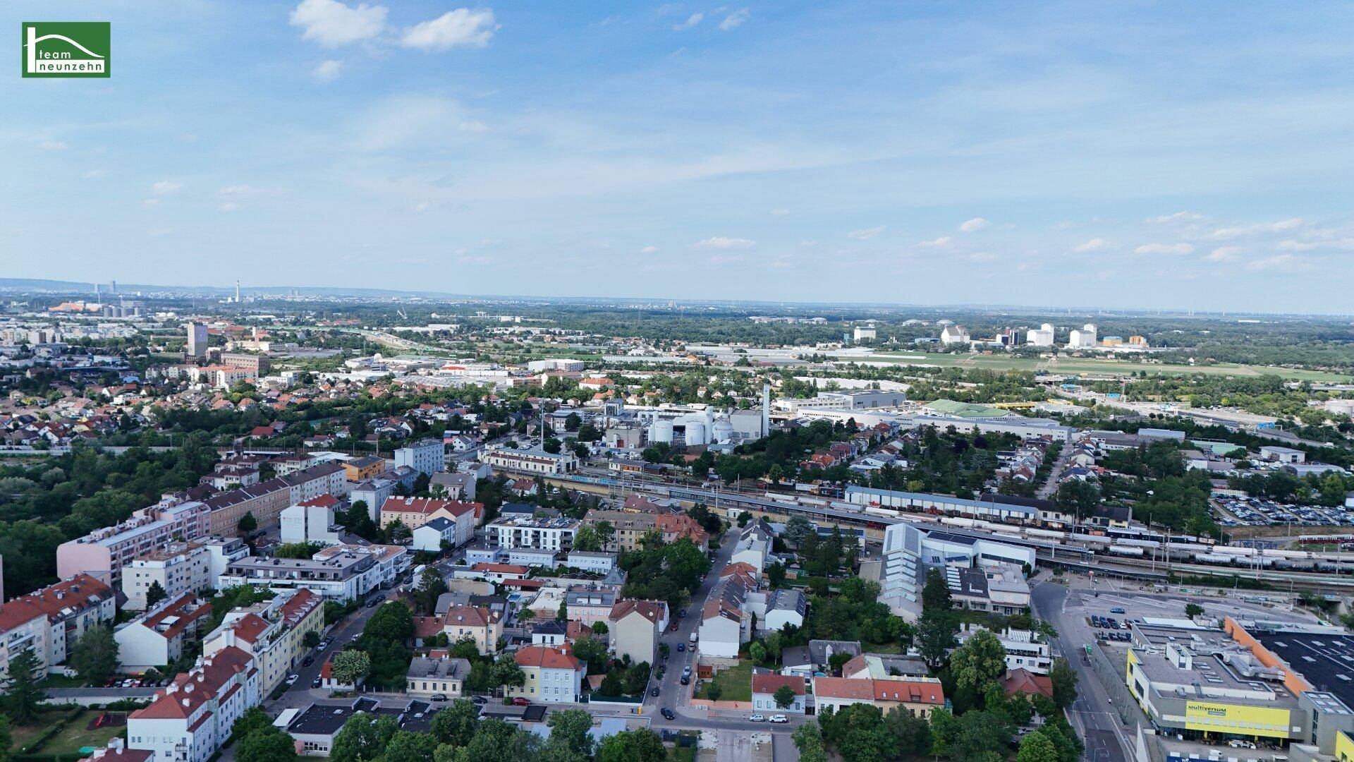 Weitläufige Luftaufnahme einer Stadtlandschaft mit Wohngebieten, Industrieanlagen und einer Bahnlinie.