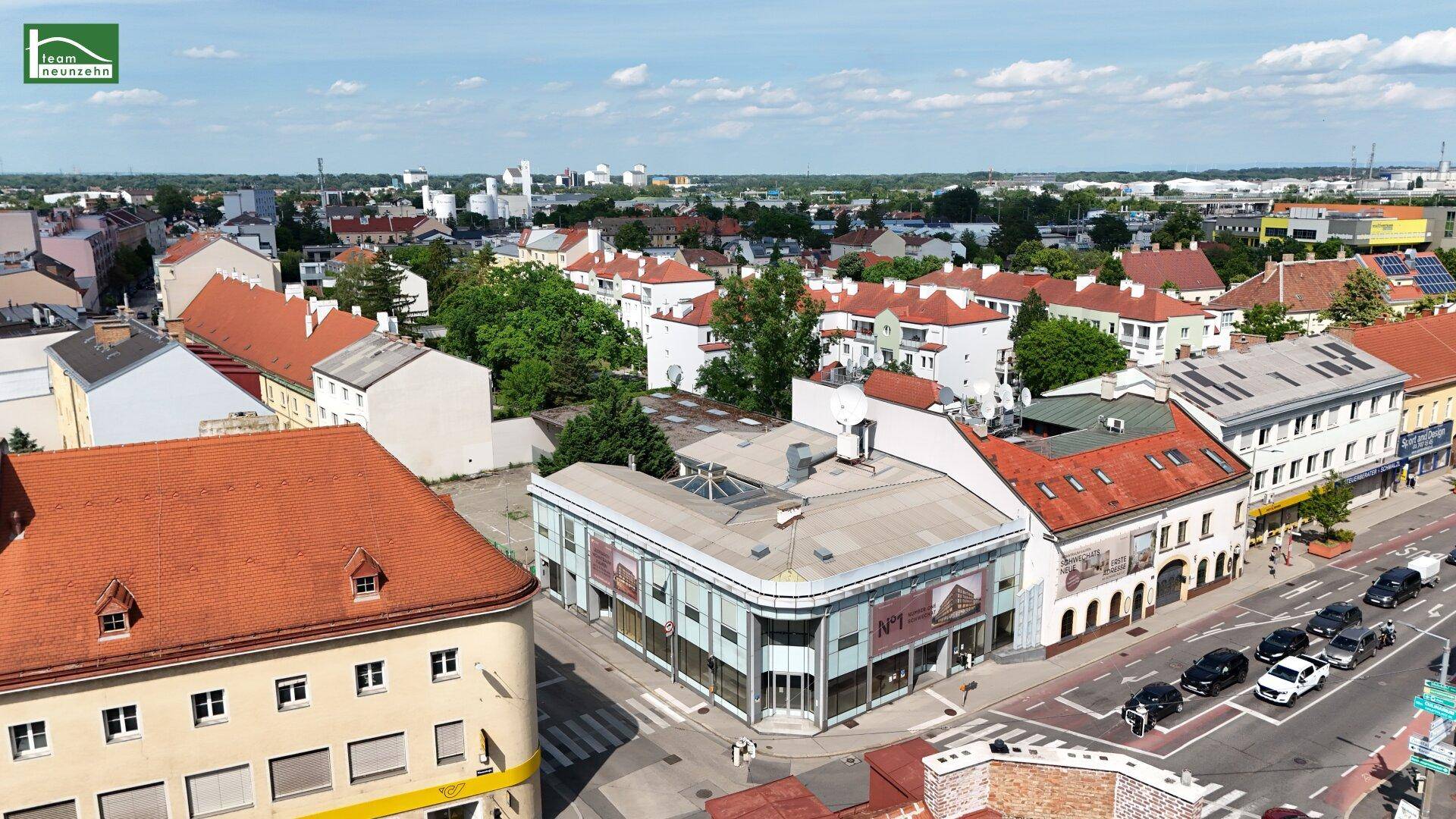 Luftaufnahme einer städtischen Kreuzung mit Gebäuden und Dächern unter blauem Himmel.