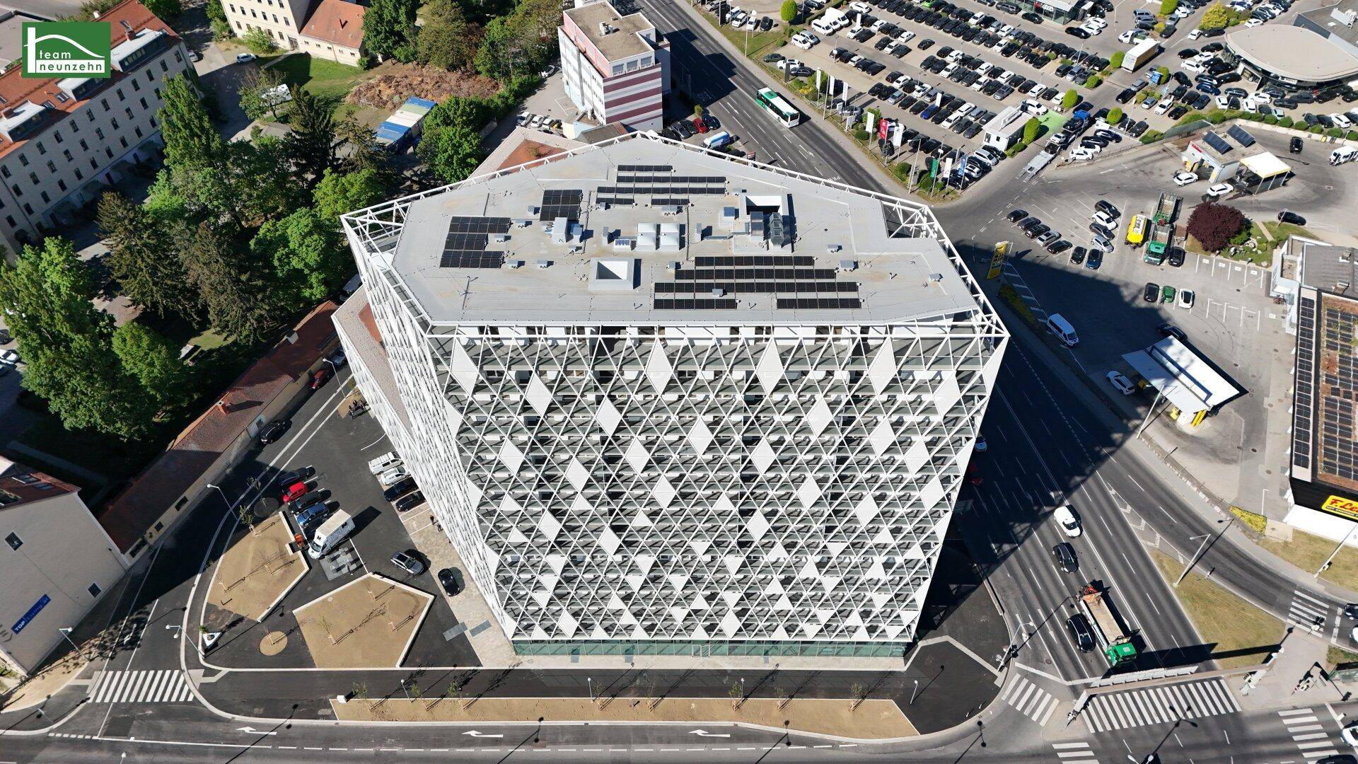 Panoramablick von oben auf ein markantes, modernes Gebäude mit weißer Gitterfassade und Solaranlage in urbaner Landschaft.