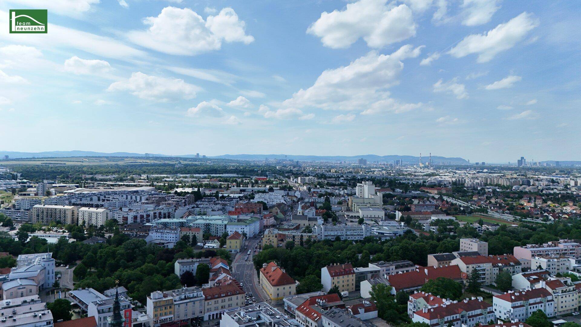 Weitläufige Luftaufnahme einer Stadtlandschaft mit Blick auf die umliegenden Hügel und den blauen Himmel.