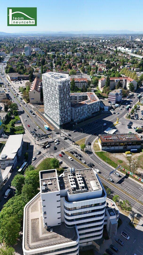 Panoramische Luftaufnahme der Stadt mit einem markanten modernen Gebäude und weitreichendem Blick über die grüne Umgebung.