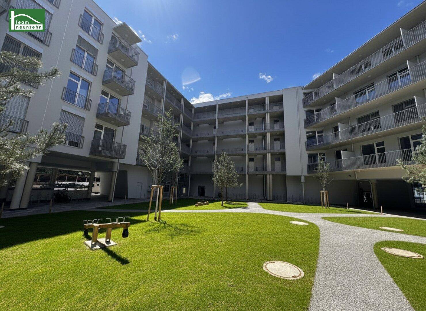 Begrünter Innenhof einer Wohnanlage mit Spielgerät und Rasenflächen, umgeben von modernen Gebäuden.