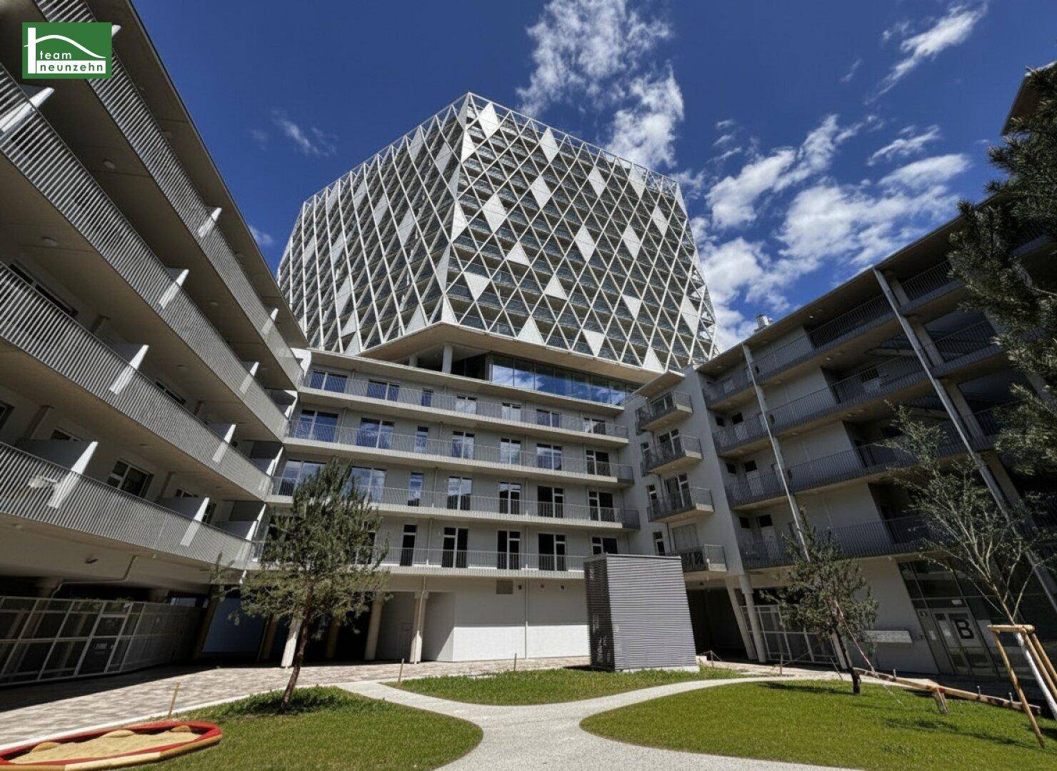 Innenhof eines modernen Wohnkomplexes mit Grünflächen und umliegenden Gebäuden mit Balkonen.