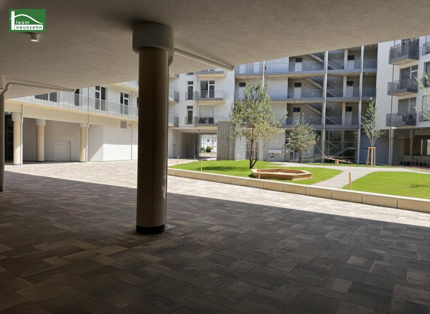 Überdachter Außenbereich mit Säulen und gepflastertem Boden im modernen Wohnkomplex.