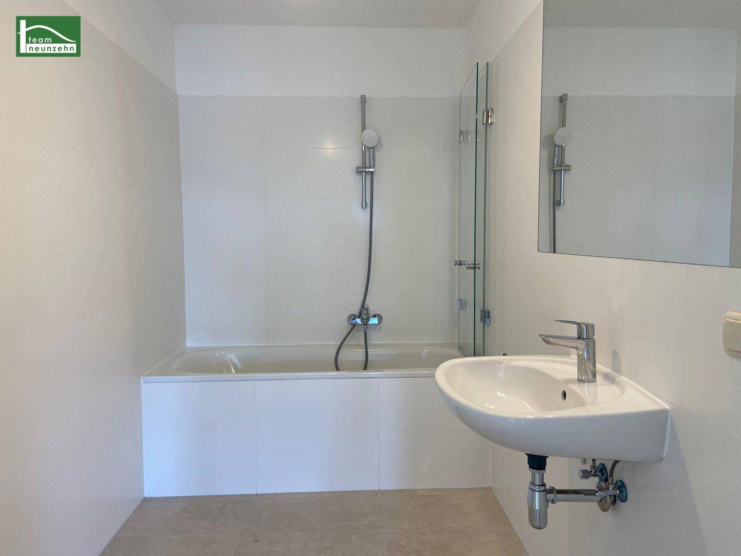 Modernes Badezimmer mit Badewanne, Duschvorrichtung, Waschbecken und weißen Fliesen.