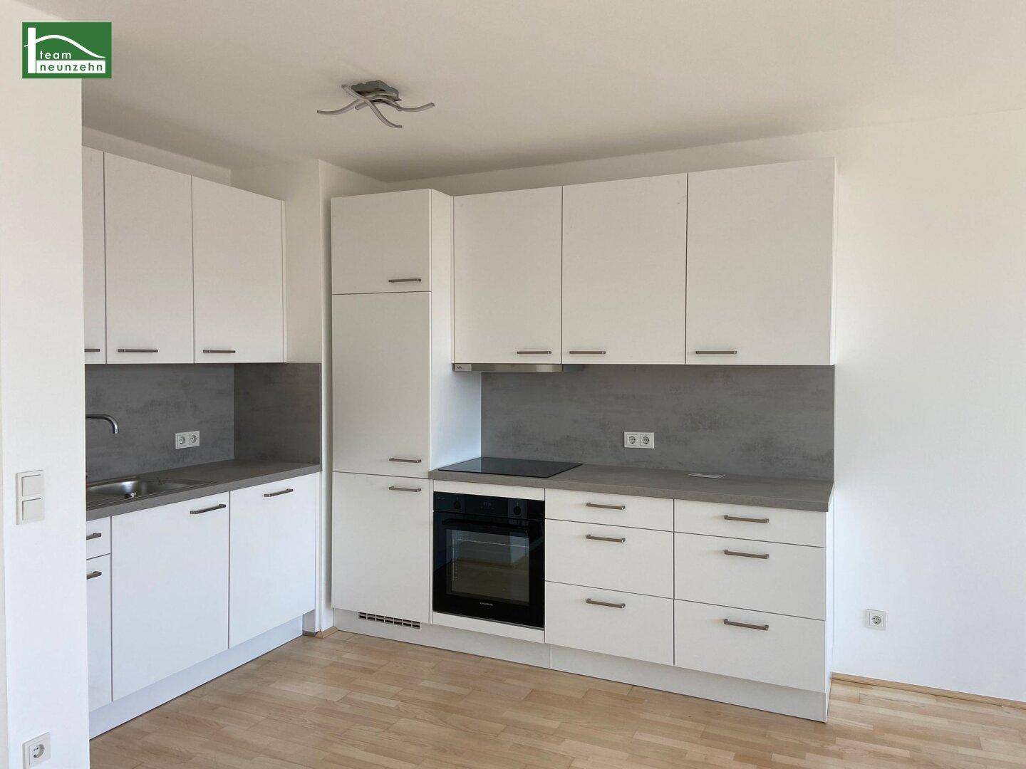 Moderne Einbauküche mit weißen Schränken, grauer Arbeitsplatte und integrierten Geräten.