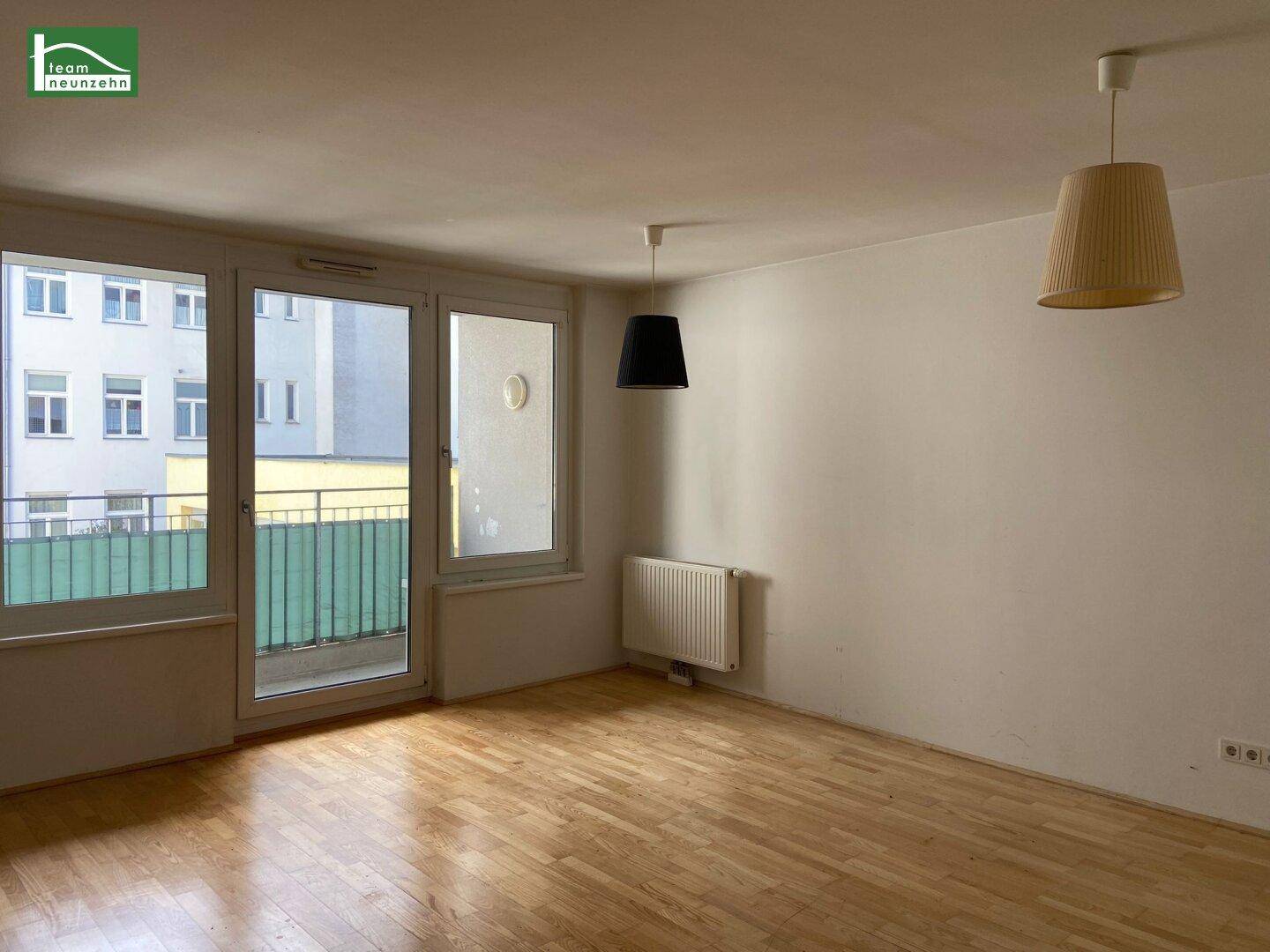 Helles Wohnzimmer mit Parkettboden, Heizkörper und Zugang zu einem kleinen Balkon.