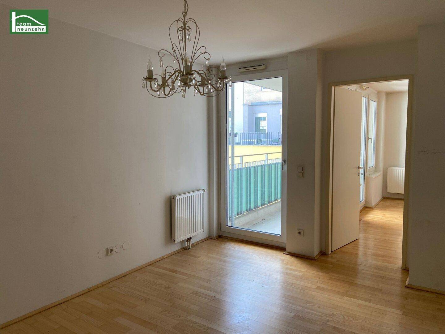 Wohnbereich mit Parkettboden, Kronleuchter und Zugang zu einem Balkon, der viel Licht spendet.