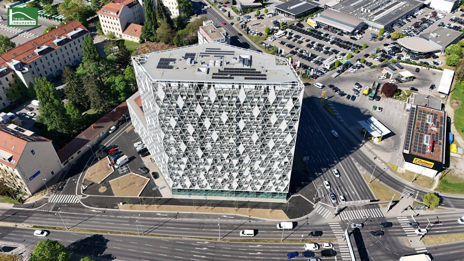 Draufsicht auf ein zeitgenössisches Gebäude mit auffälliger Fassadenstruktur und Solarpaneelen im Stadtgebiet.