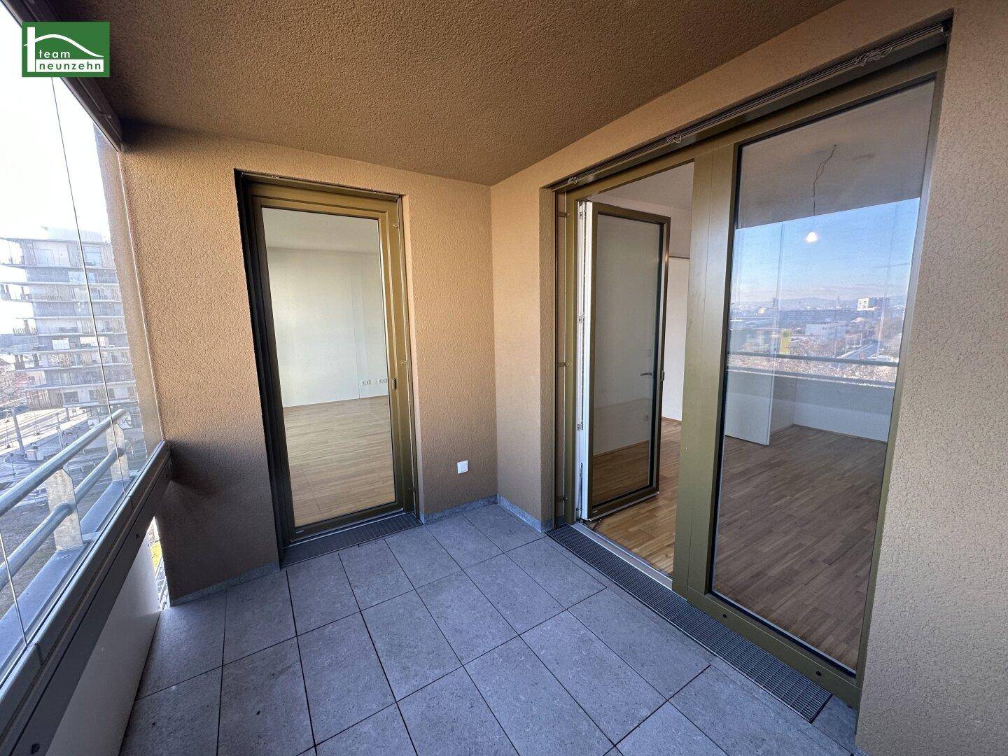 Geräumiger Balkon mit Fliesenboden, Glasbrüstung und weitem Stadtblick.