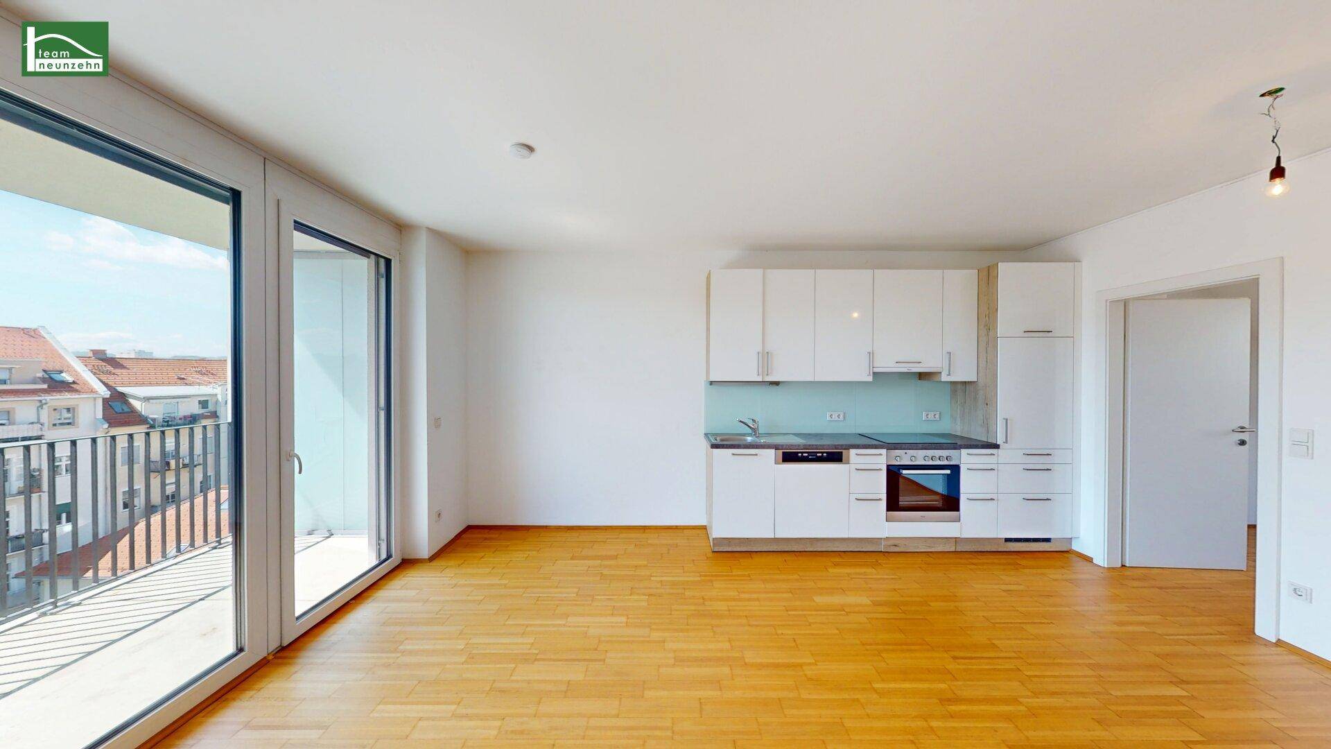 Heller Wohnbereich mit Holzboden, Zugang zum Balkon und integrierter Küchenzeile.
