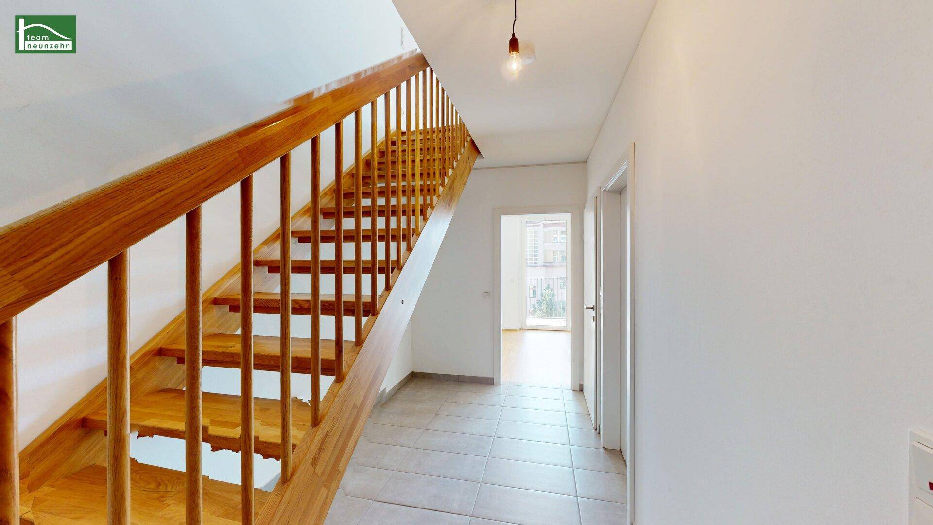 Geräumiger Flur mit Holztreppe und Fliesenboden, der zu den oberen Etagen führt.