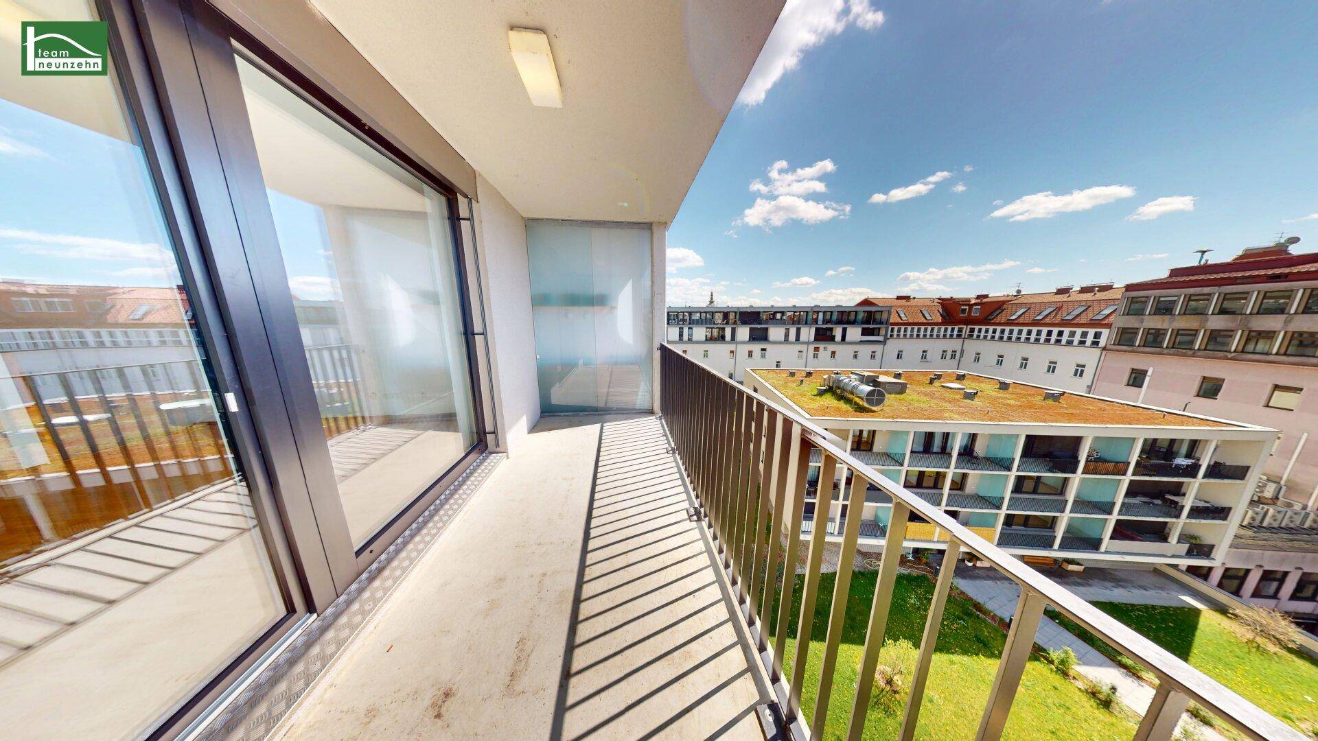 Geräumiger Balkon mit Metallgeländer und Blick auf umliegende Gebäude und Grünflächen.