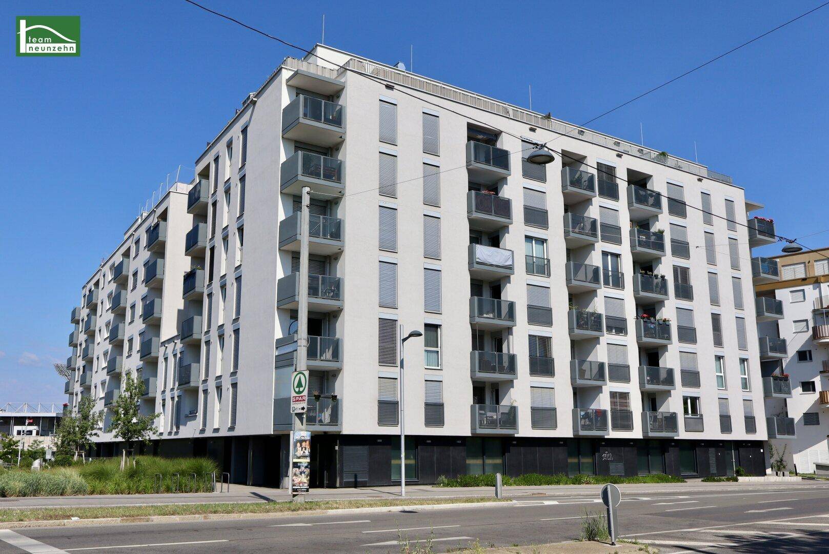 Moderne Wohnanlage mit mehreren Etagen, Balkonen und großen Fenstern an einer Straße.
