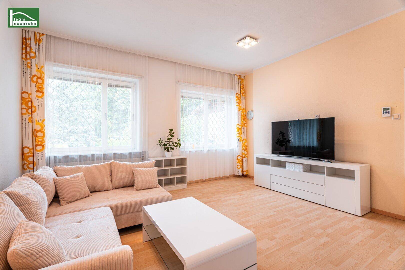 Gemütliches Wohnzimmer mit beigem Sofa, hellem Parkett und einem modernen TV-Möbel.