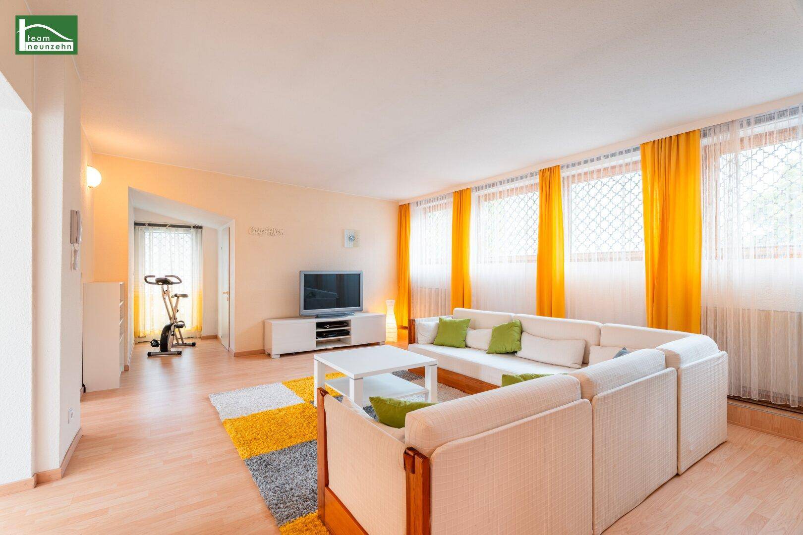 Helles Wohnzimmer mit großem Sofa, hellem Parkettboden und Blick auf den Trainingsbereich.