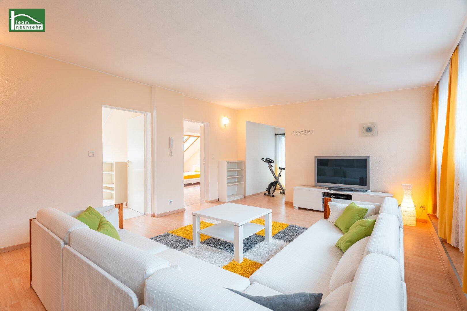 Geräumiges Wohnzimmer mit großem Ecksofa, hellem Parkett und farbenfrohem Teppich.