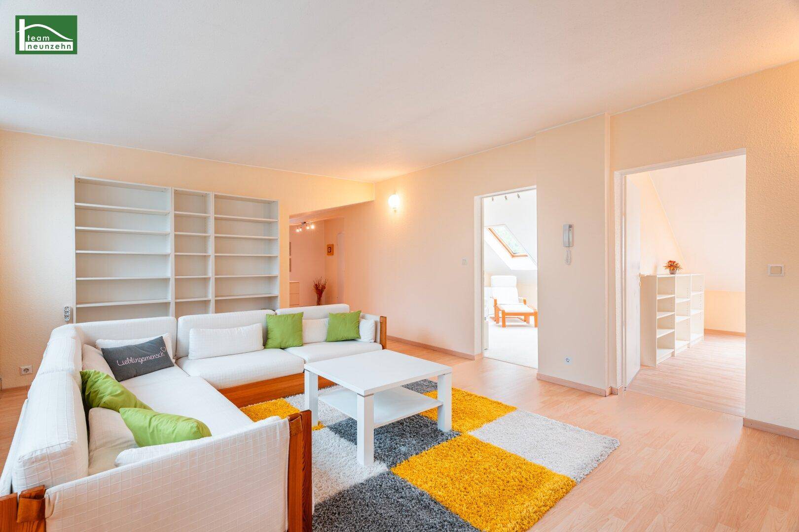 Offener Wohnbereich mit großem Sofa, Bücherregalen und Zugang zu weiteren Räumen.