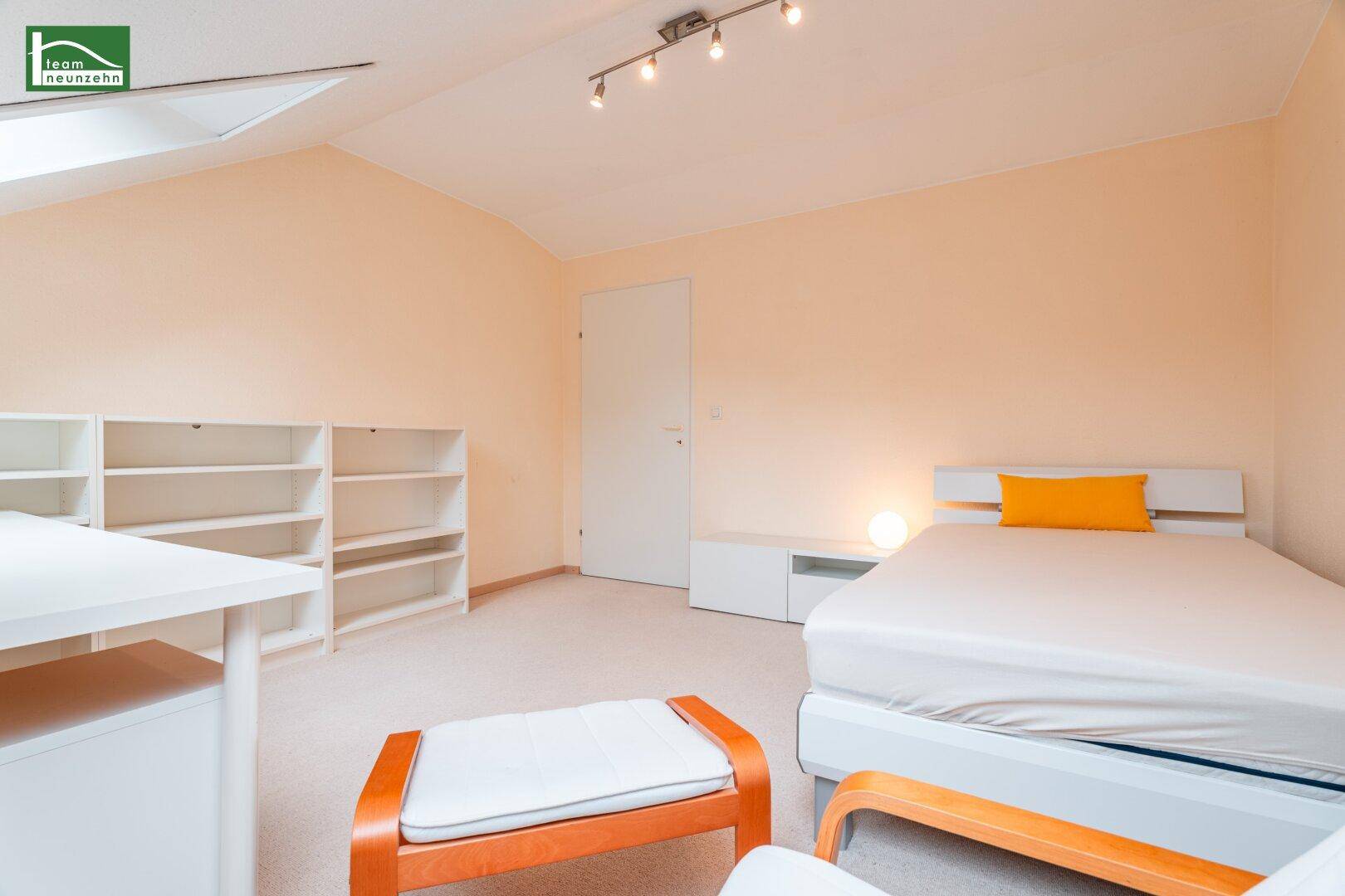 Helles Dachgeschoss-Schlafzimmer mit Teppichboden, Bett und Schreibtischbereich.