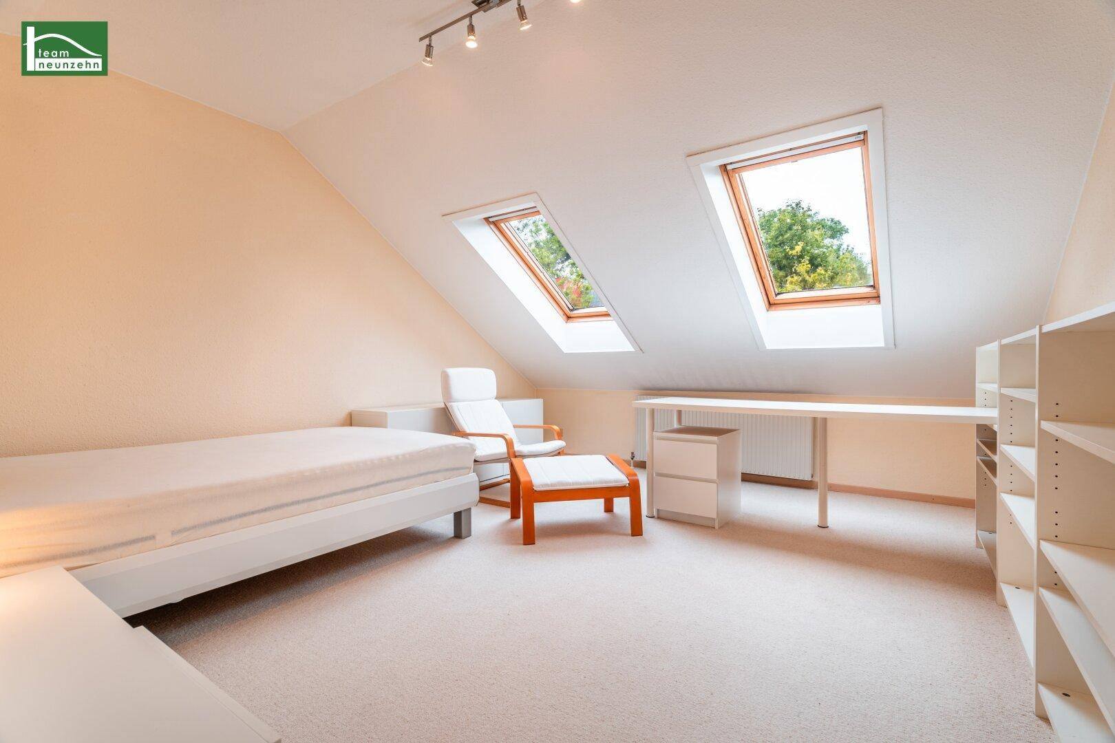 Geräumiges Dachgeschoss-Schlafzimmer mit Schreibtisch, Sessel und zwei Dachfenstern.