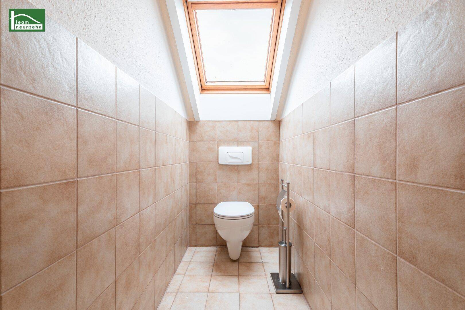 Separates WC im Dachgeschoss mit beigefarbenen Fliesen und einem Dachfenster für Tageslicht.