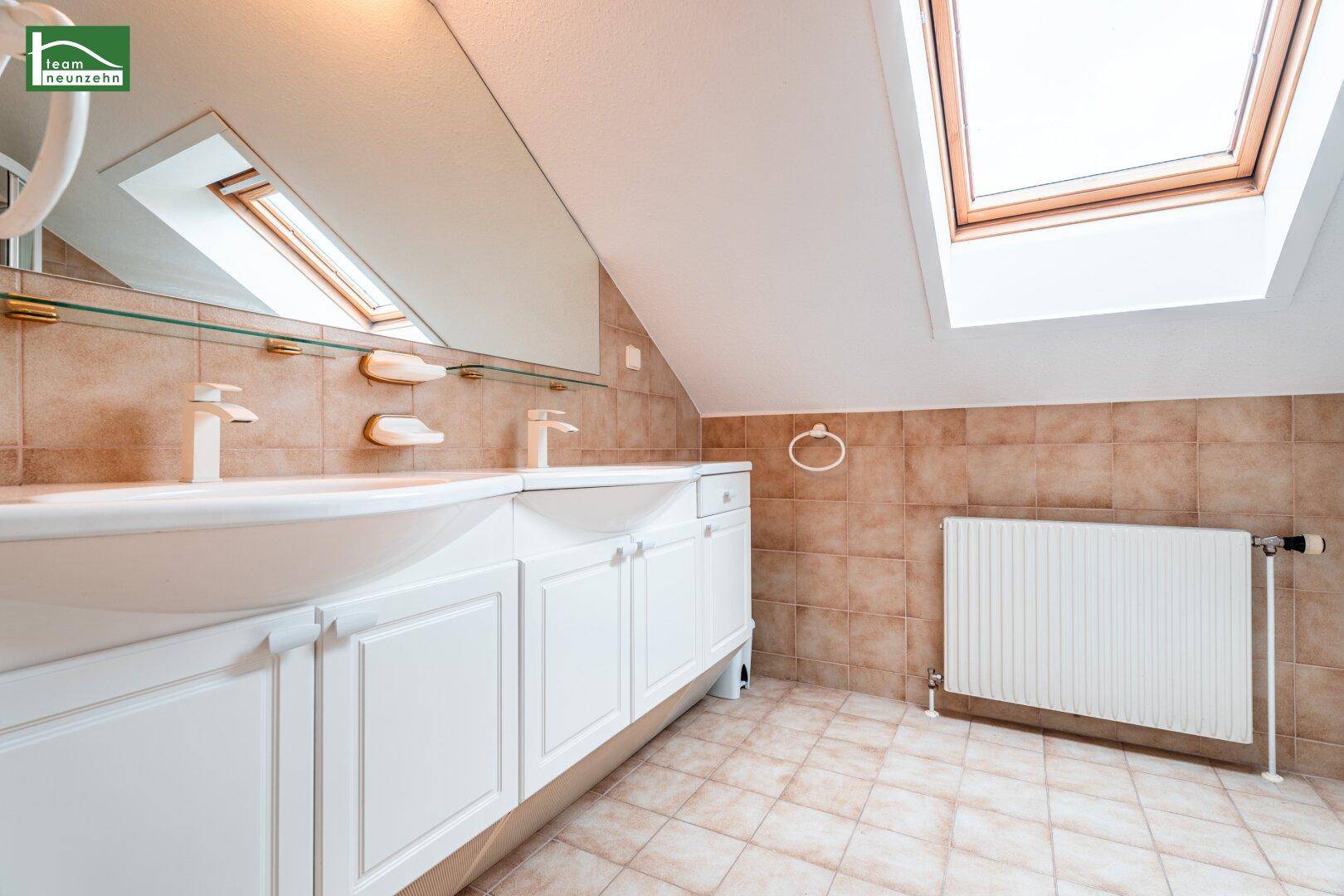 Badezimmer im Dachgeschoss mit Doppelwaschbecken, Spiegelschrank und Dachfenster.