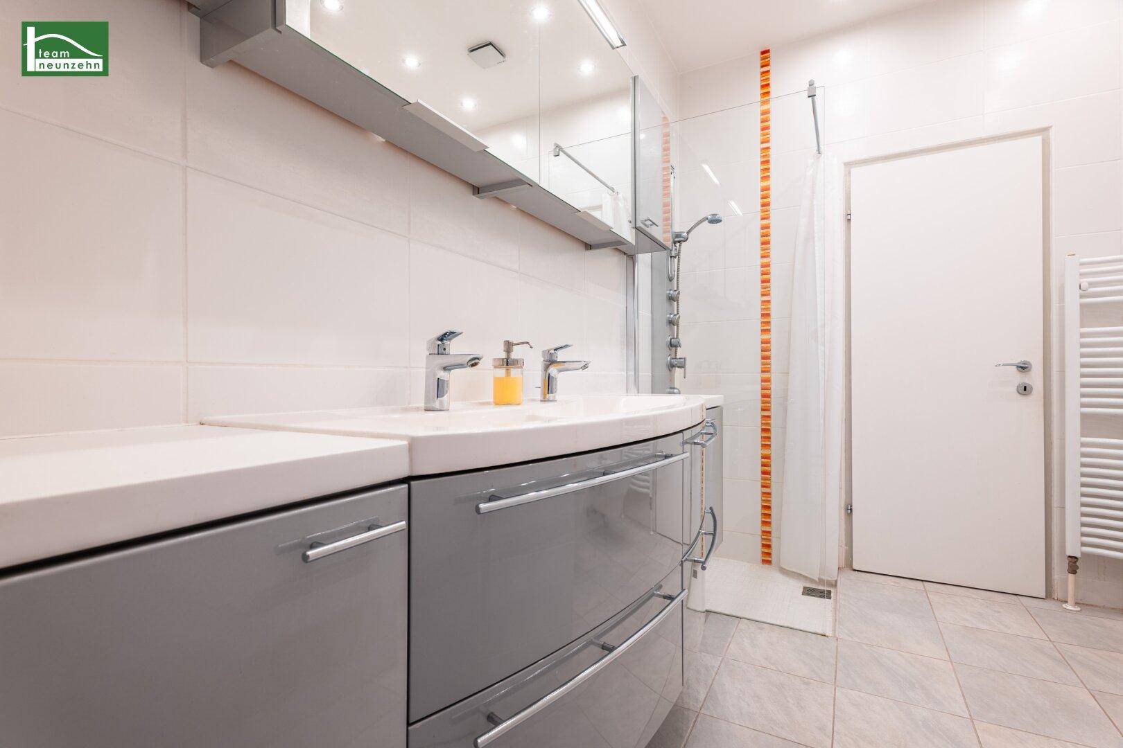Modernes Badezimmer mit Doppelwaschbecken, großem Spiegel und begehbarer Dusche in hellen Farben.