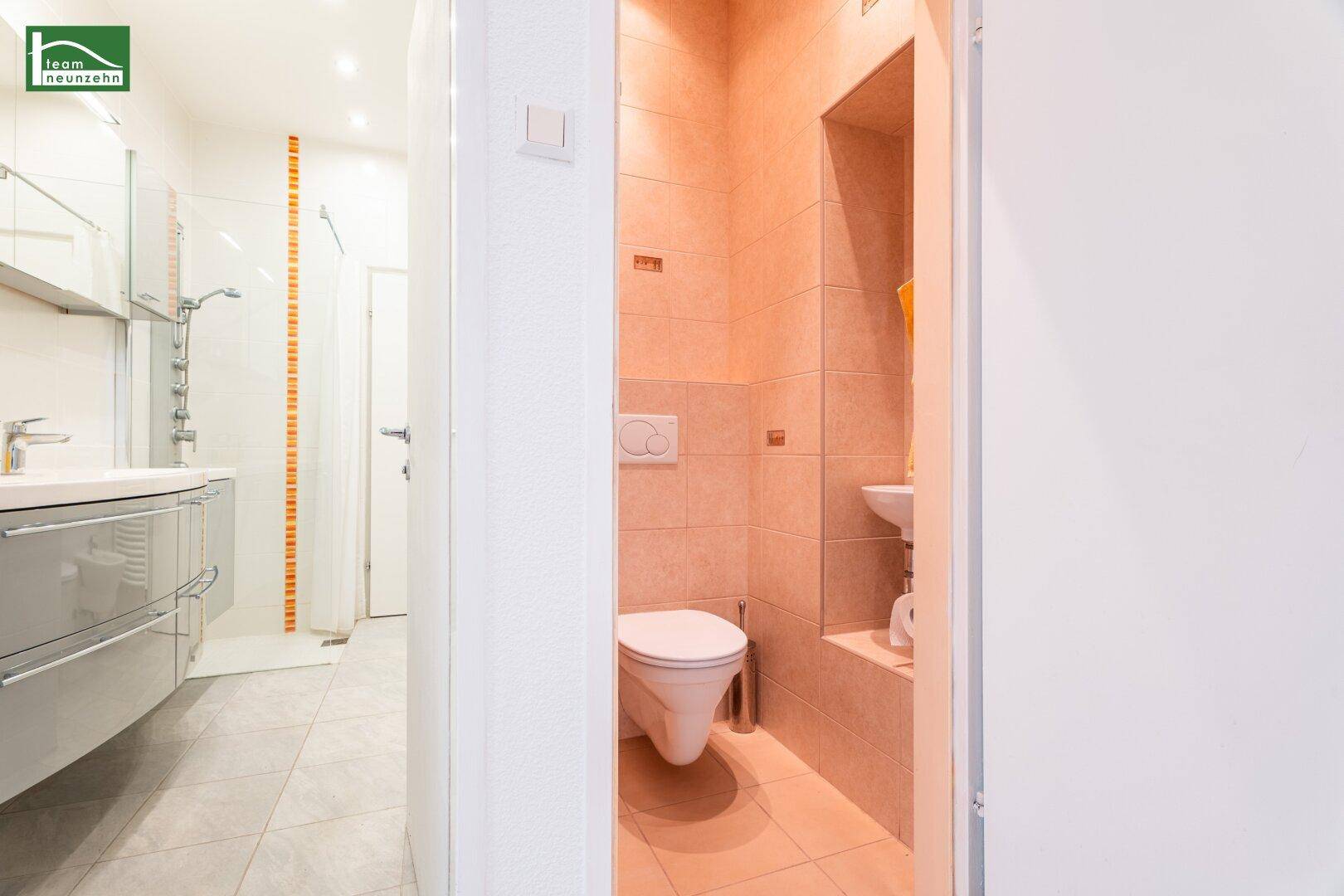 Blick vom Flur in ein modernes Badezimmer mit Doppelwaschbecken und eine separate Gästetoilette.