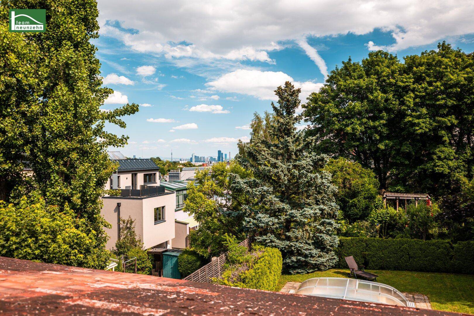 Panoramablick über einen grünen Garten mit Liegestuhl und die Dächer der Stadt in der Ferne.