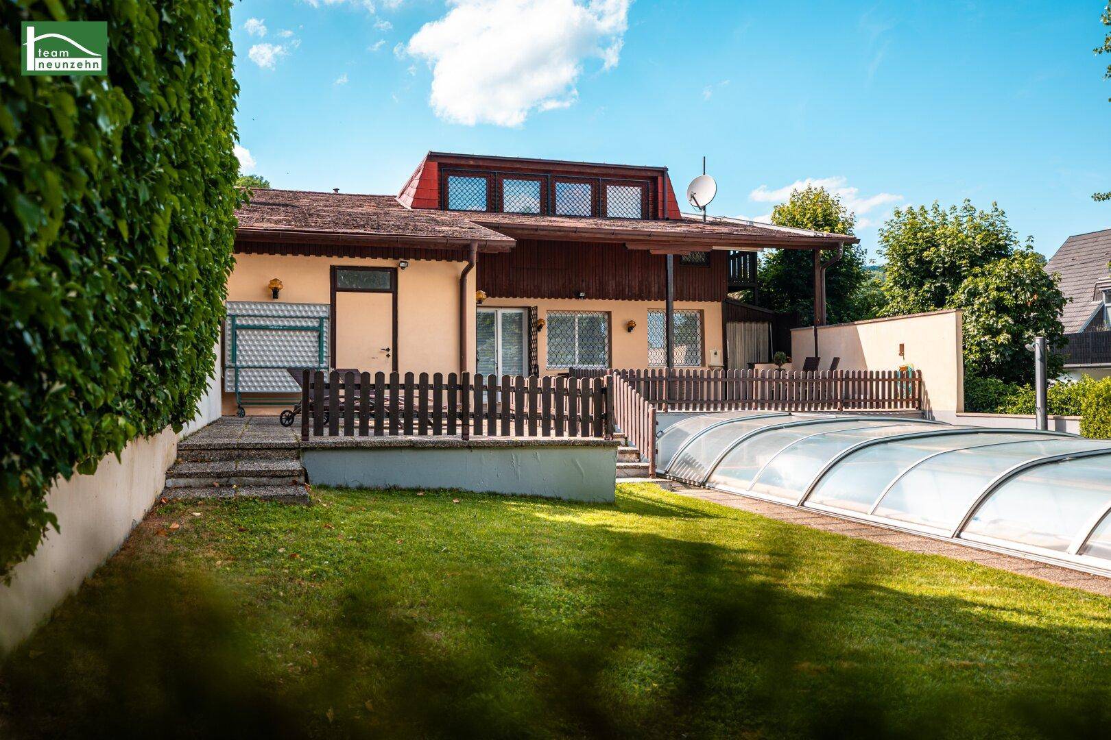 Rückansicht des Hauses mit großem Garten, überdachtem Pool und Terrasse im Obergeschoss.