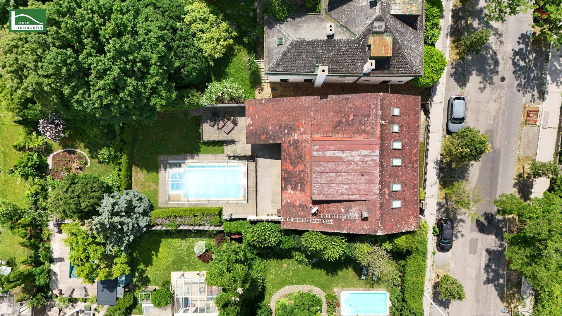 Luftaufnahme des Anwesens mit Haus, Swimmingpool und umliegenden Gärten sowie der angrenzenden Straße.