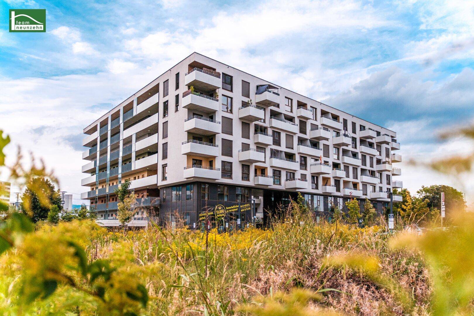 Modernes Wohngebäude mit vielen Balkonen, umgeben von natürlicher Vegetation.