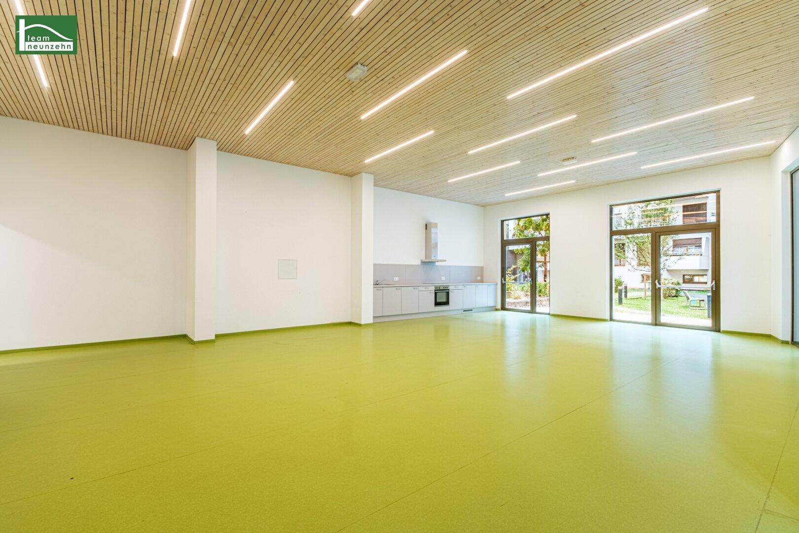 Großer Gemeinschaftsraum mit Holzdecke, moderner Beleuchtung und integrierter Küchenzeile.