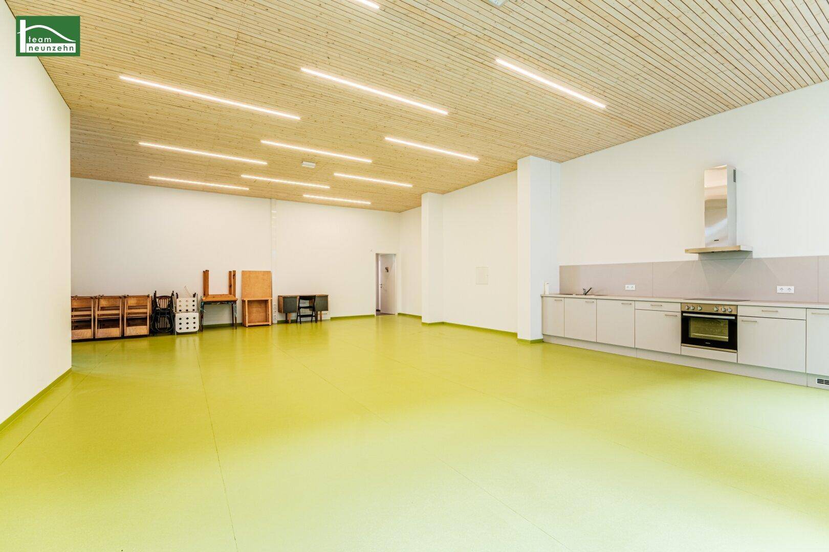 Geräumiger Gemeinschaftsraum mit heller Holzdecke, funktionaler Küchenzeile und viel Platz.