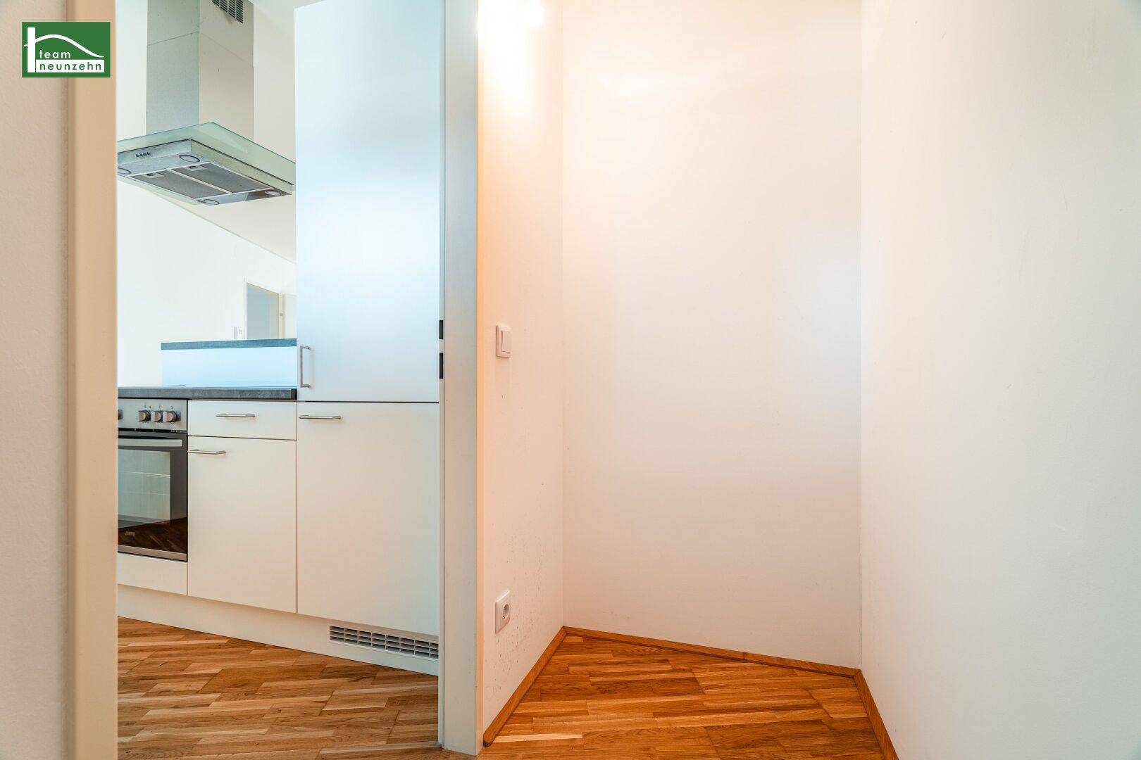 Blick von einem Flur in die moderne Küche mit Holzboden und Dunstabzugshaube.