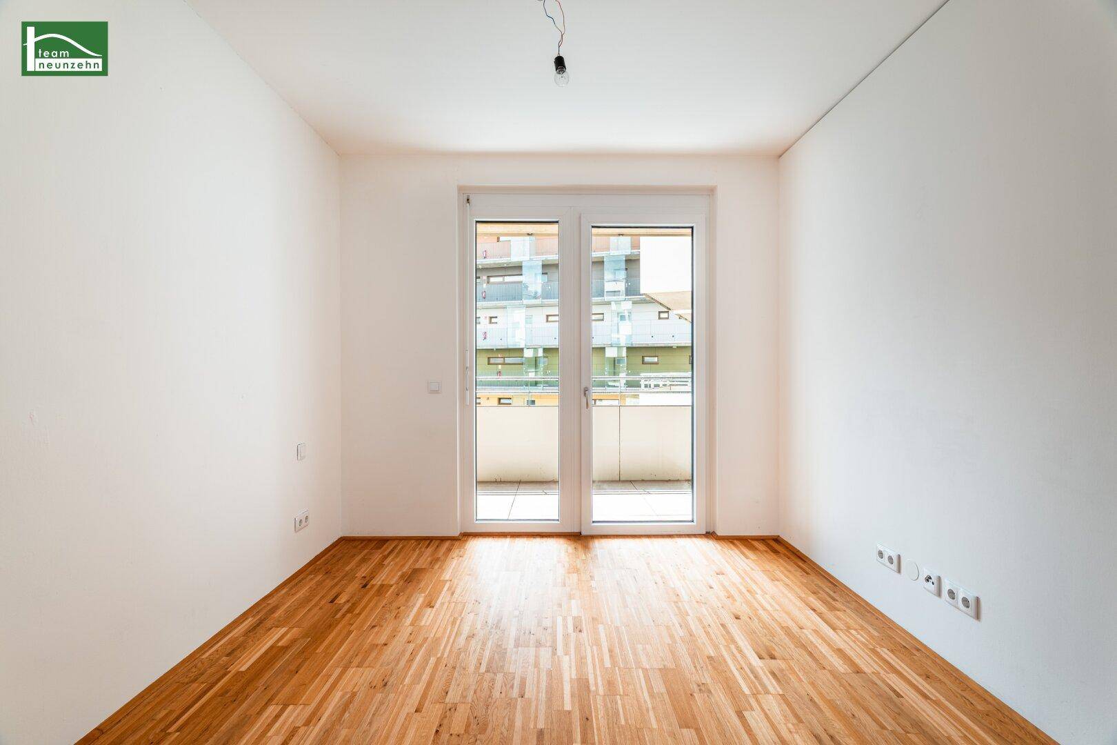 Helles Schlafzimmer mit Parkettboden und Zugang zu einem Balkon.