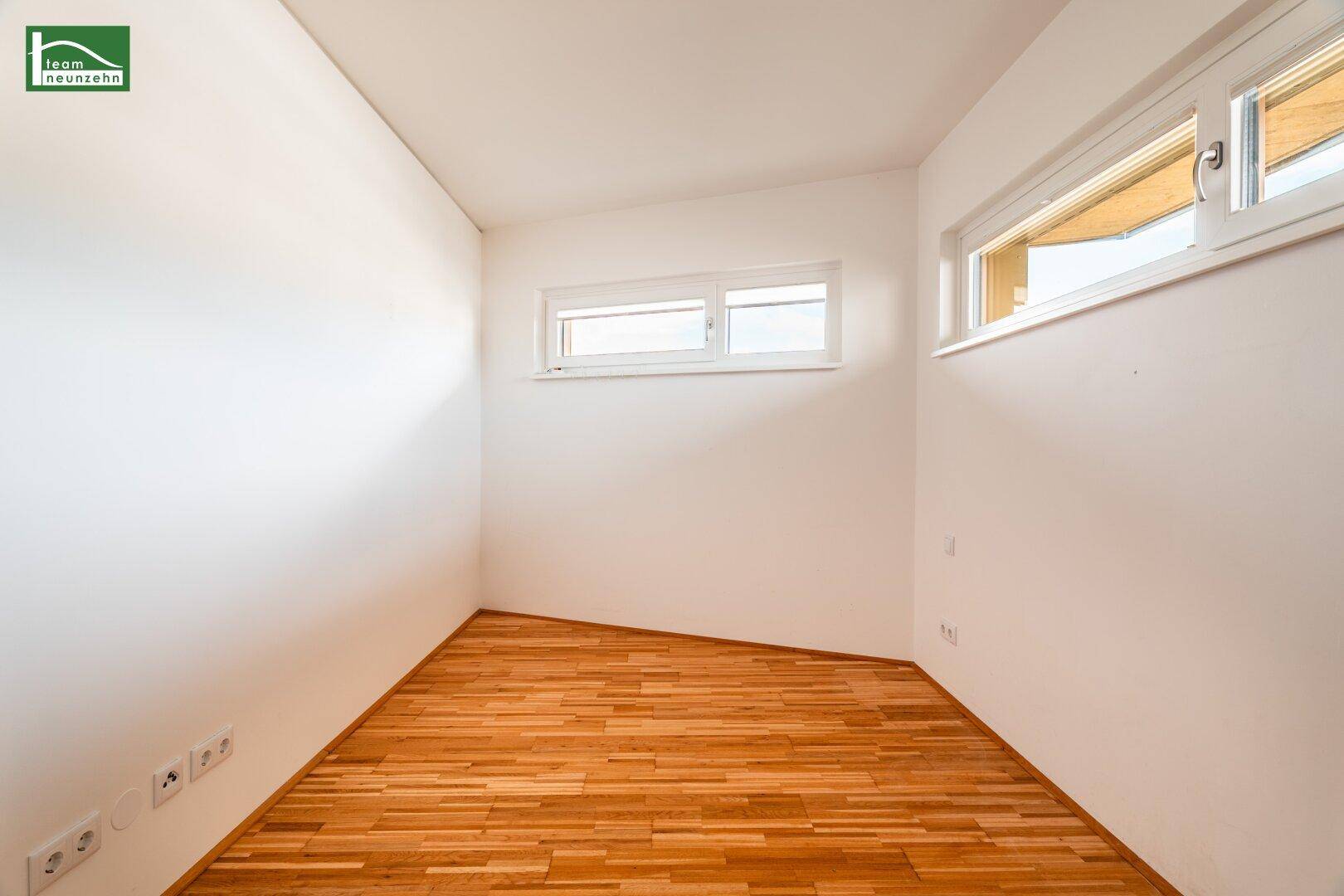 Helles Zimmer mit Parkettboden und hohen, schmalen Fenstern.