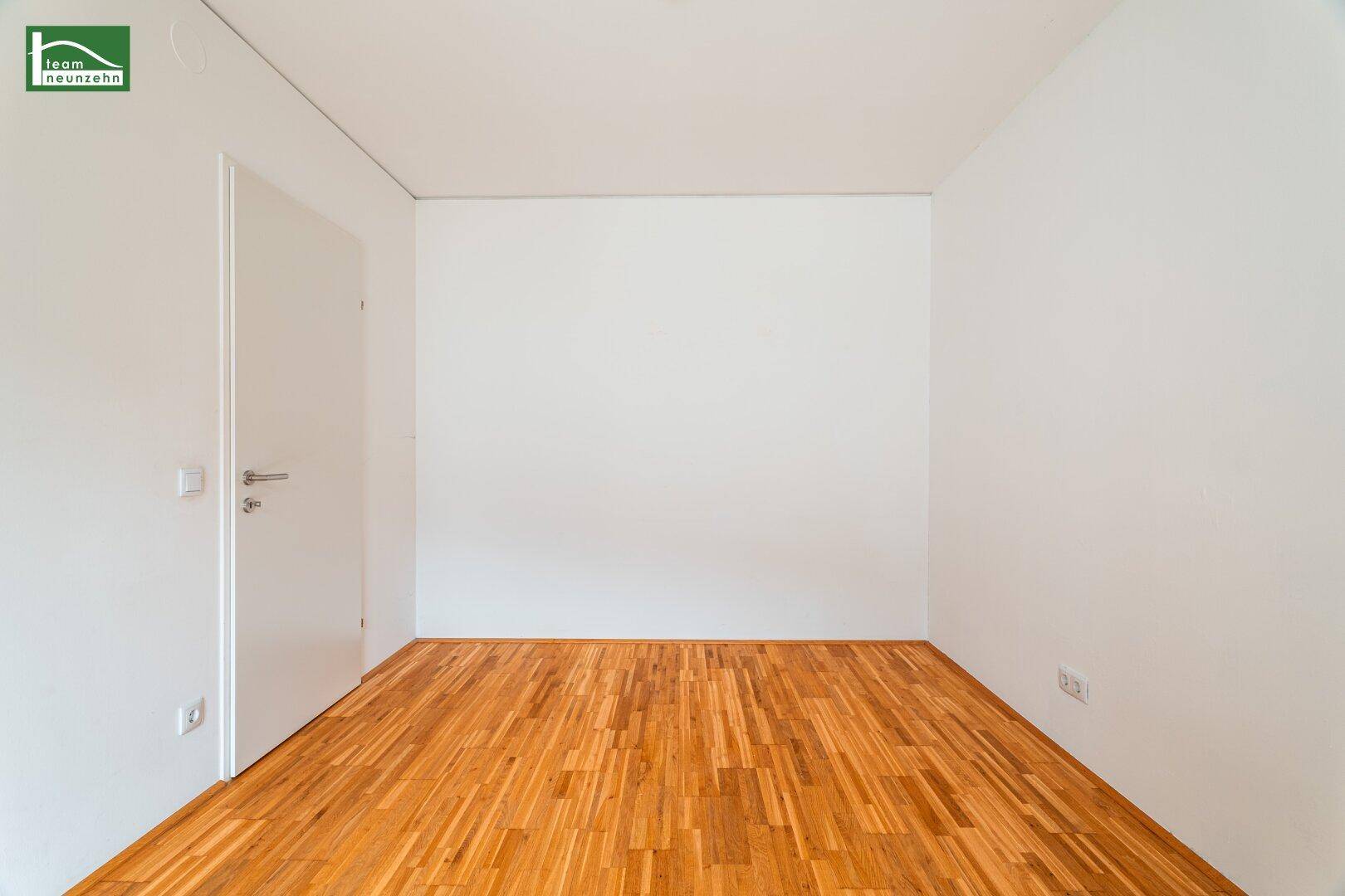 Leeres Zimmer mit Parkettboden und weiß gestrichenen Wänden.