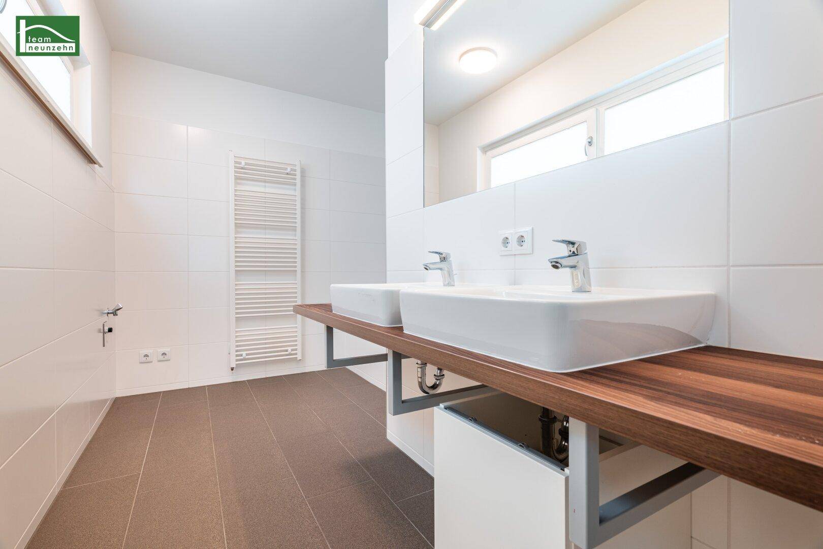 Modernes Badezimmer mit Doppelwaschbecken, Holzablage und beheiztem Handtuchhalter.