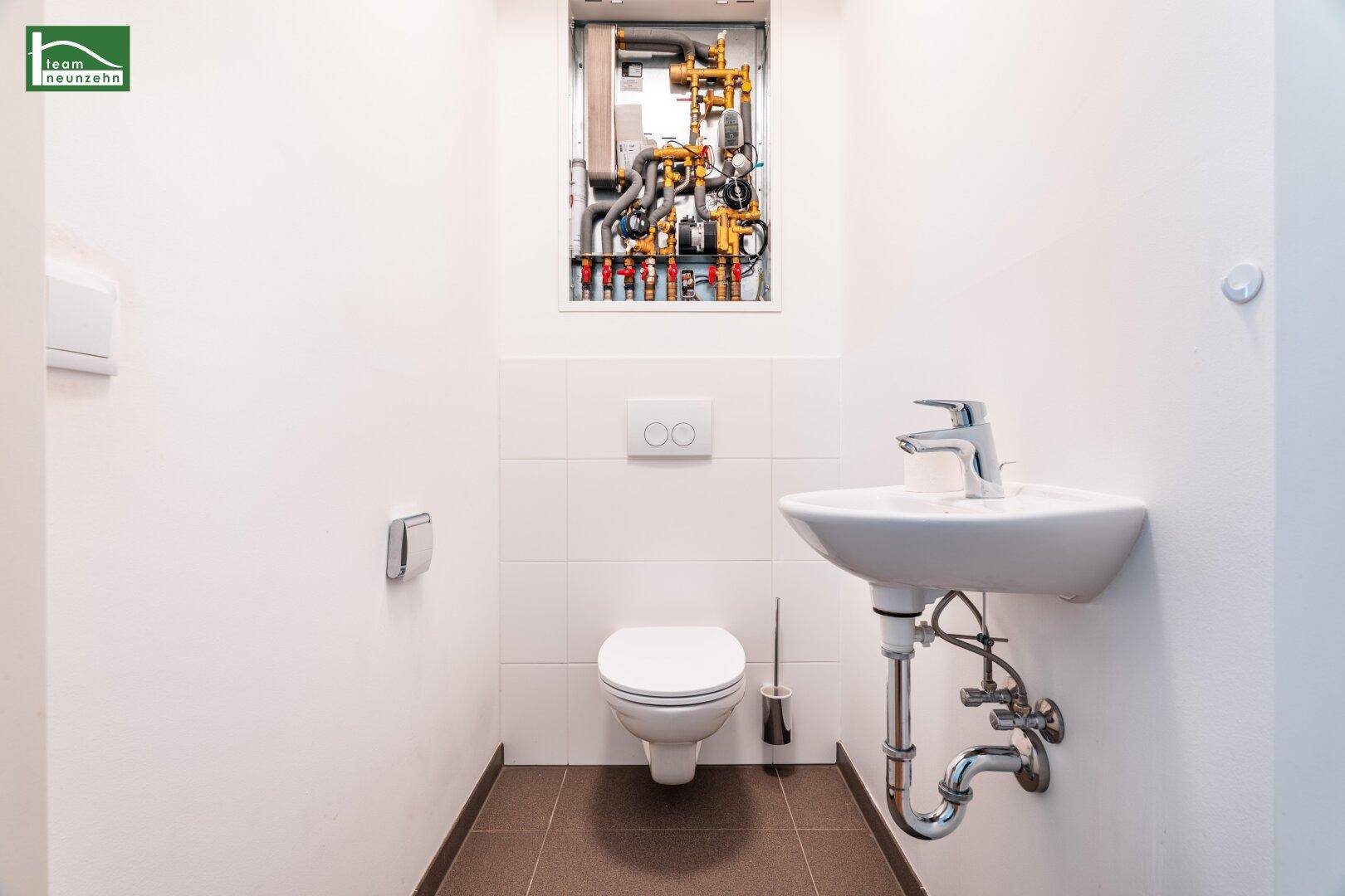 Gäste-WC mit wandhängender Toilette, kleinem Waschbecken und Heizungsverteiler.