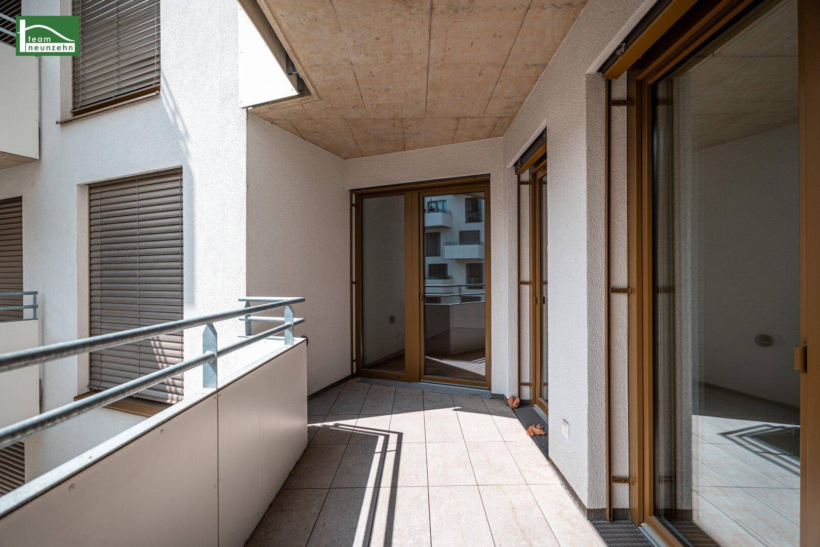 Heller Balkon mit Fliesenboden und großen Fenstertüren, die ins Innere führen.