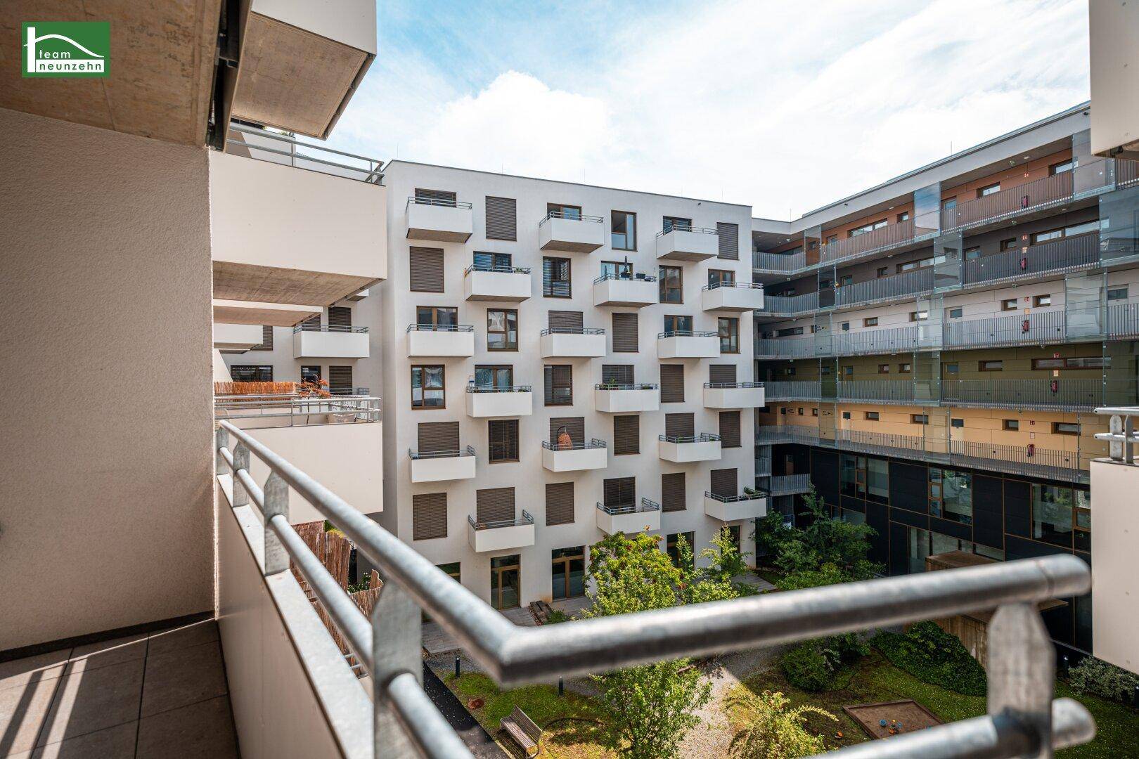 Balkon mit Blick auf den begrünten Innenhof und die moderne Wohnanlage.
